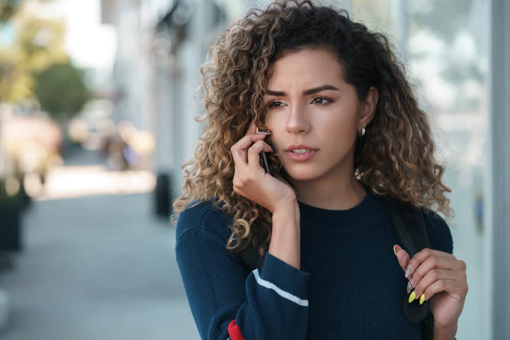 A stylish female with long hair is wearing a blue sweater and press-on fingernails, talking about hair loss with a friend.