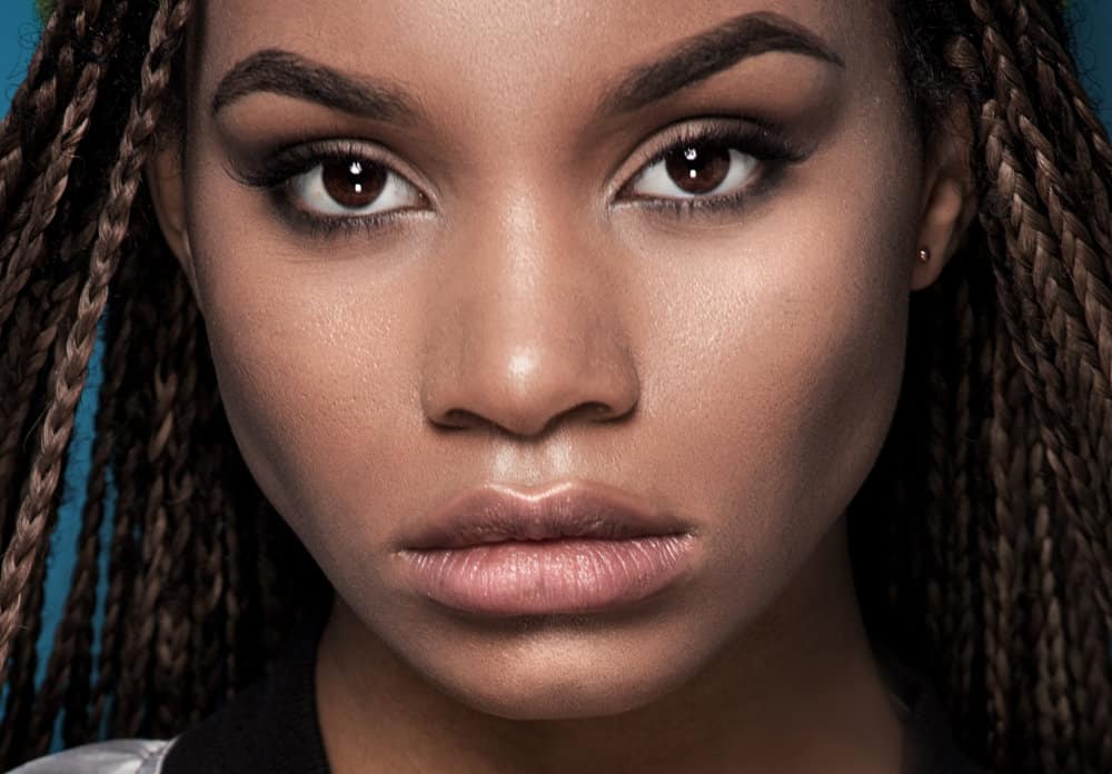 A young beautiful black girl is wearing ancient tribal braids with hair extensions and interesting patterns.