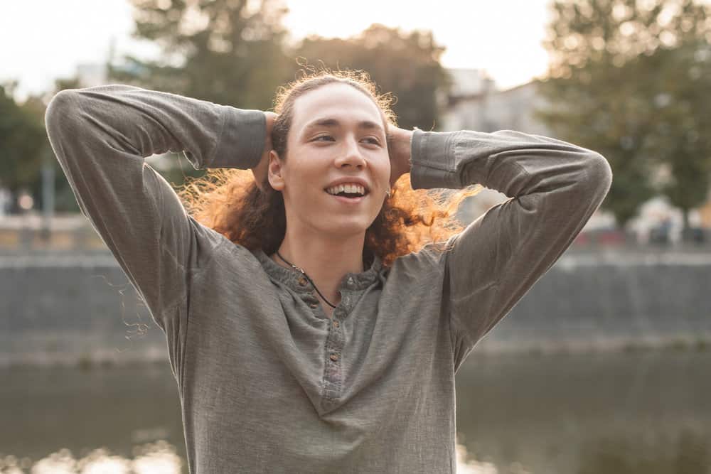 A man with long hair is pulling his wolf haircut into a trendy ponytail.