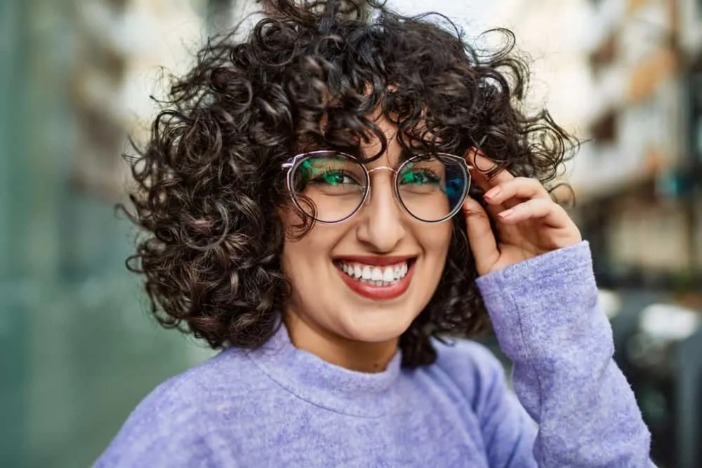 A confident young female with a great smile wearing stylish glasses after treating her dry and damaged hair.