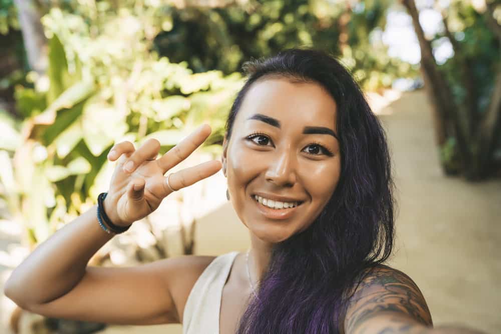 Asian female with a great smile has chemically lightened hair that's been treated with purple shampoo.