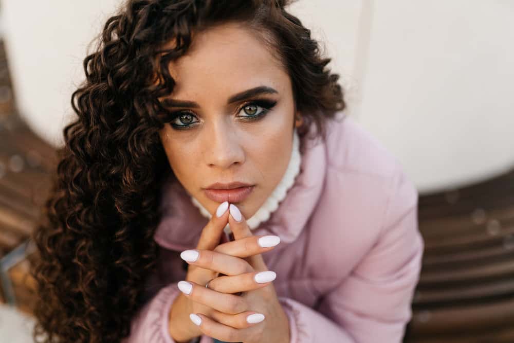 A lady with beautiful eyes has dark brown hair is wearing a spiral perm hairstyle and a light purple jacket.