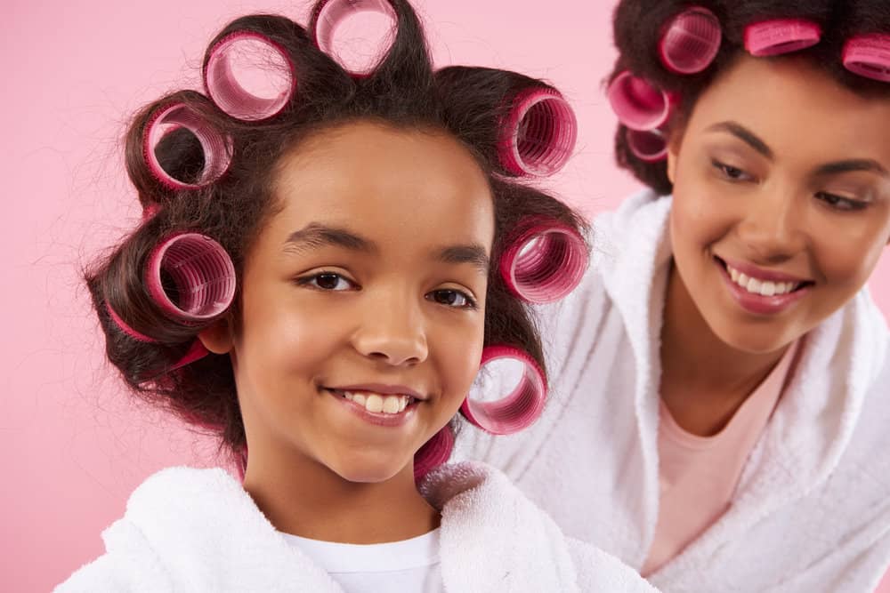 A beautiful mother and daughter using foam rollers on naturally straight hair to create bouncy, smaller curls.