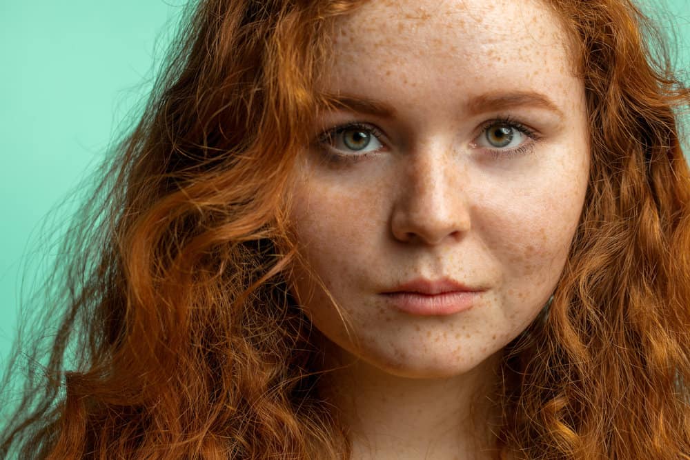 The young woman with freckles and a red natural hair color has dry hair and hair breakage.