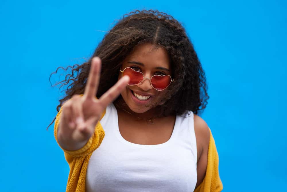 A cute young black girl that used a rosemary rinse for improved hair and scalp health is making a peace sign.