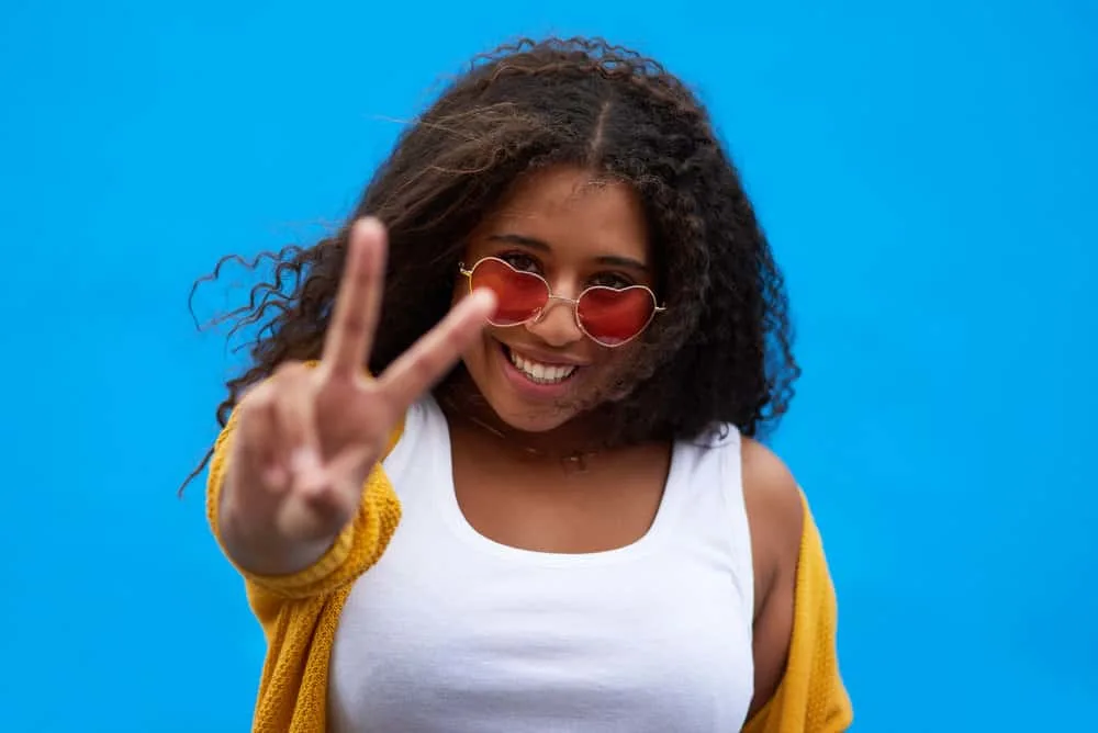 A cute young black girl that used a rosemary rinse for improved hair and scalp health is making a peace sign.