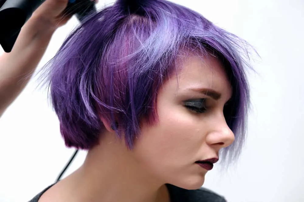 Bisexual Bob Haircut: What Is the Bi Bob? Step-By-Step Tutorial 6 A cute white girl in the queer community is getting her shorter hair styled into a bob hairstyle.