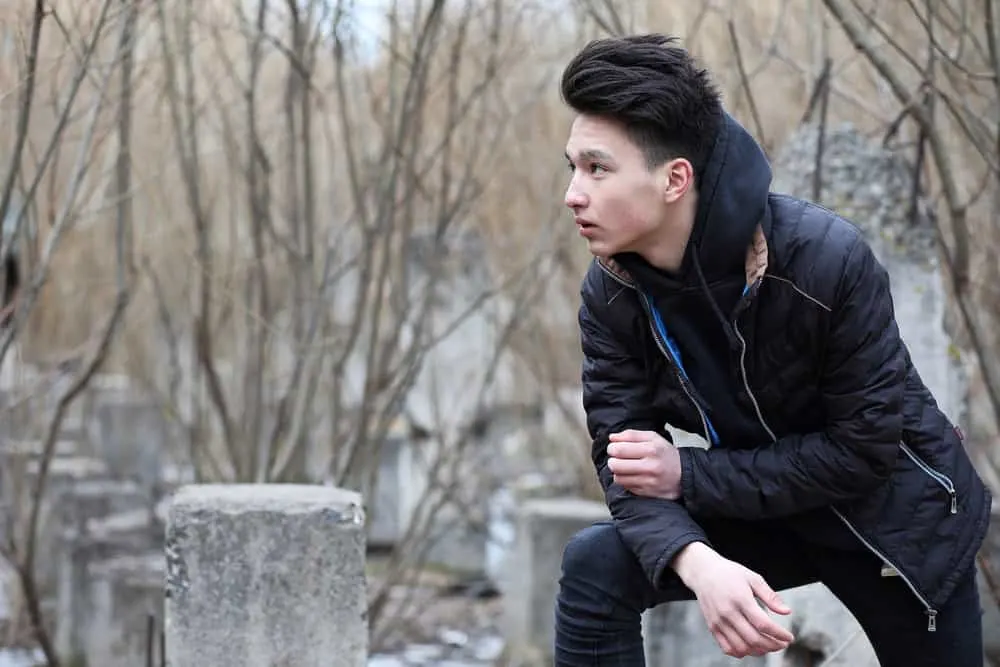 The Best K-Pop Hairstyles for Korean Guys (Plus Styling Tips) 7 Asian man outside wearing a Kpop-inspired style with a buzz cut on the side and extra length on top.