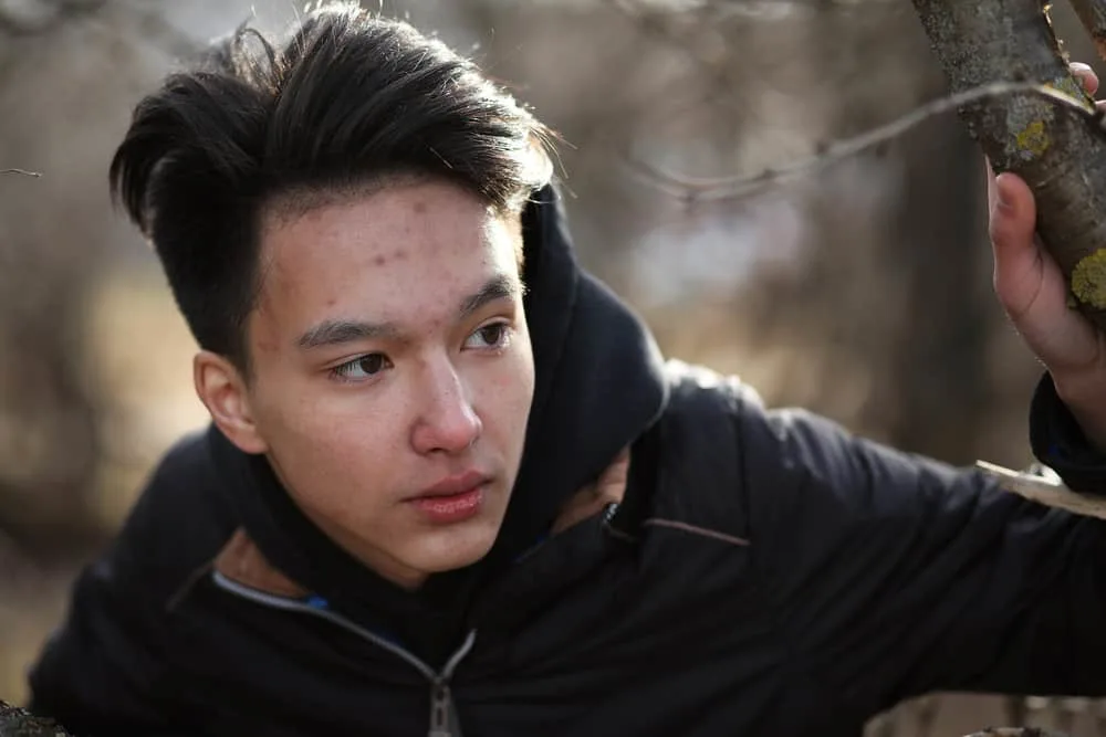 A male wearing a popular Kpop hairstyle with his hair trimmed short on the sides and longer hair on the top.
