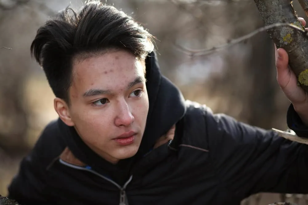 The Best K-Pop Hairstyles for Korean Guys (Plus Styling Tips) 4 A male wearing a popular Kpop hairstyle with his hair trimmed short on the sides and longer hair on the top.