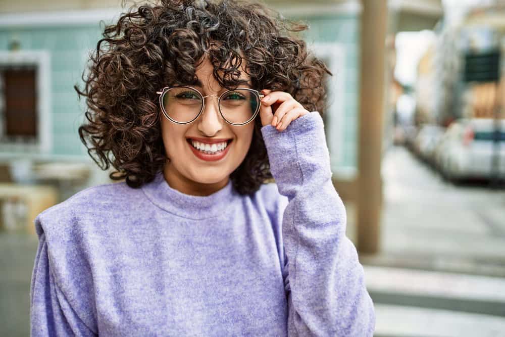 A confident young woman with curly hair strands styled with a moisturizing hair spray and a wide tooth comb.