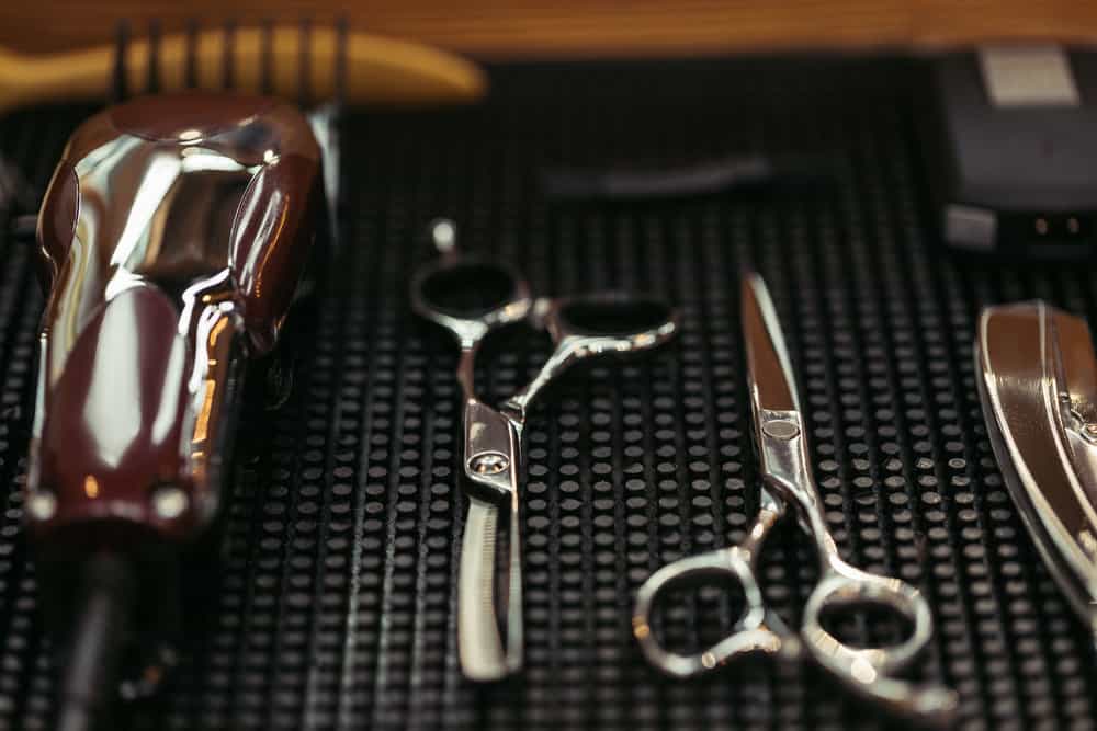 Two pairs of haircutting shears and a pair of hair clippers with a dull cutting blade sitting on a magnet holder.