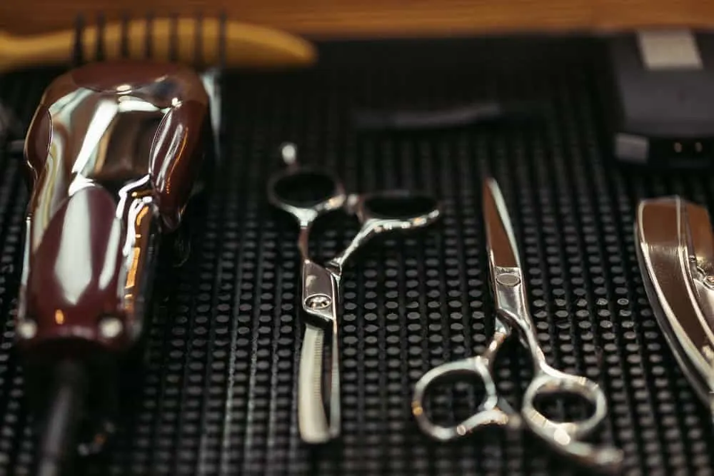 How to Sharpen Clipper Blades With and Without a Stone 8 Two pairs of haircutting shears and a pair of hair clippers with a dull cutting blade sitting on a magnet holder.