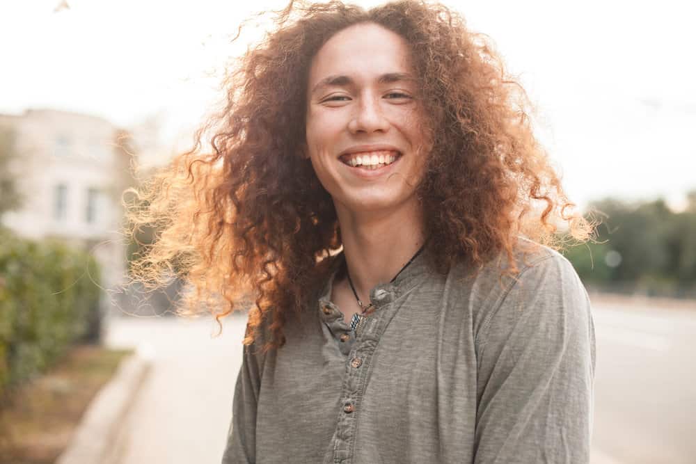 A guy with an oval face shape and curly hair texture wearing a wolf hairdo (e.g., shag cut) with extra volume.