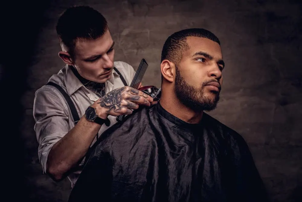 A black man getting a hair cut and special hair treatment has short hair slightly longer than a traditional buzz cut.