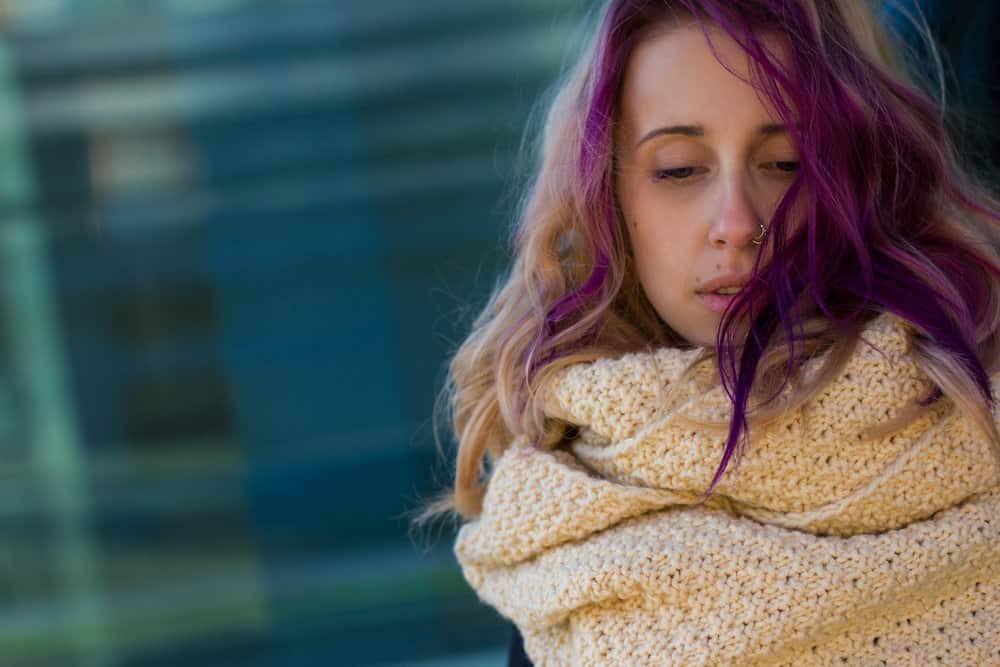 A female with dark blonde hair with purple highlights has hair color stains on her forehead.