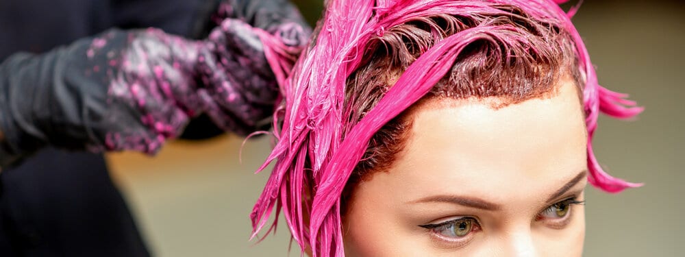 A young adult female is getting a red and pink hair dye treatment at a local Curl Centric hair salon.