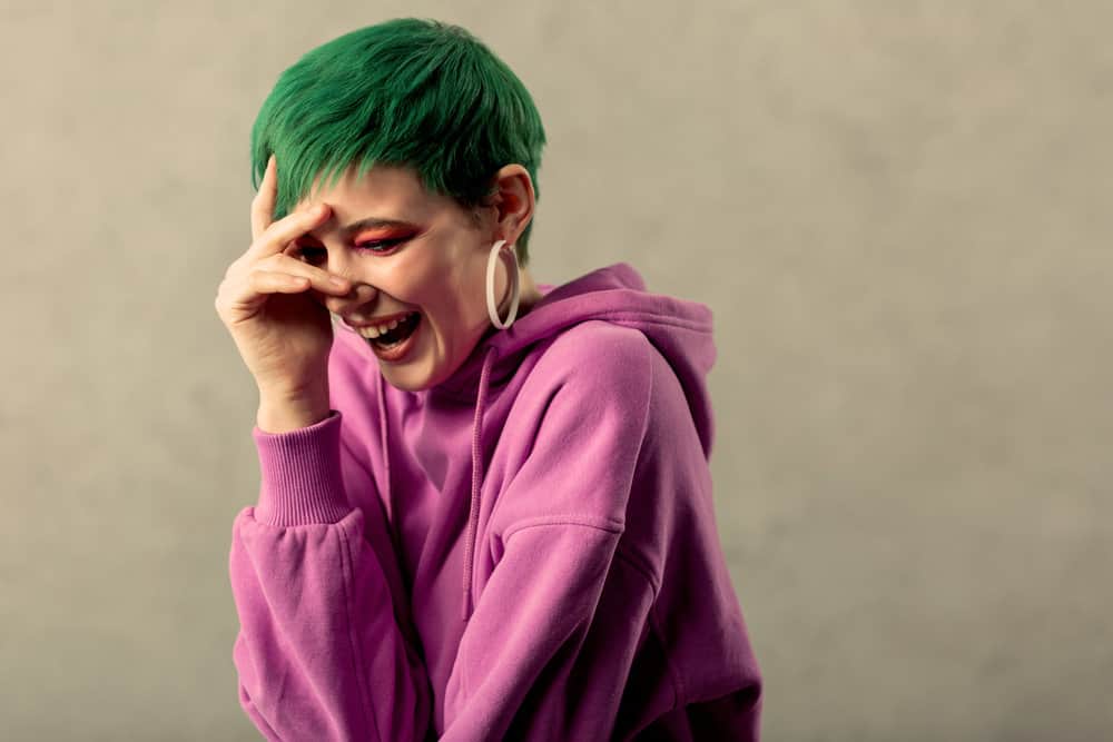 A positive woman is enjoying a laugh wearing semi-permanent dye, creating a green tinge on her straight hair strands.