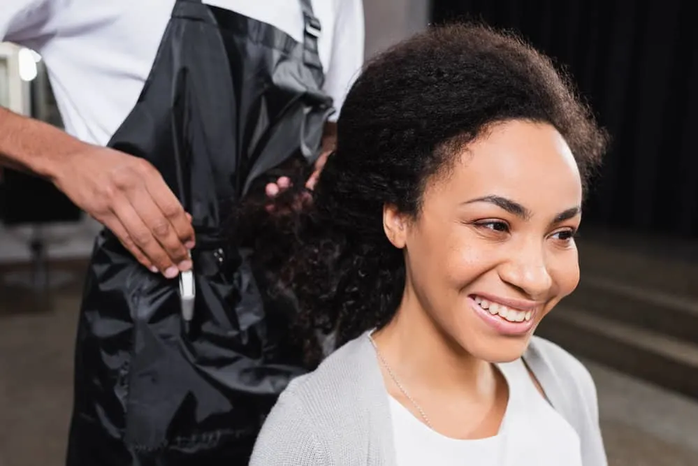 How Much Do You Tip a Hairdresser for a Haircut and More 6 African American female with frizzy type 3 hair strands is starting a hair appointment at a local hair salon.