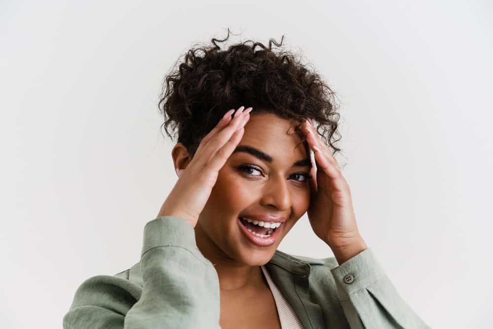 An excited young female used baking soda to clean her scalp after applying hair dye to her curly hair strands.