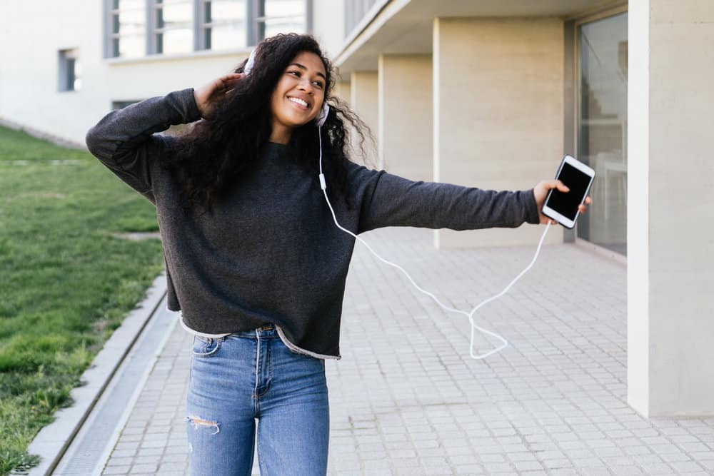 An attractive light-skinned black female is listening to a podcast about the risks of wet hair follicle damage.