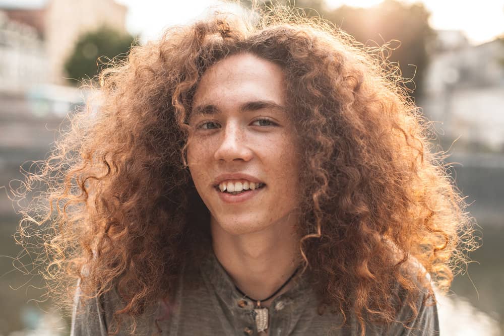 A young white male with curly, fine hair is wearing a shaggy wolf cut styled with texturizing spray on thicker hair.