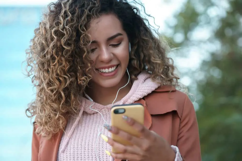 A cute female with a curly hair type has greasy hair fibers that she's discussing with a friend over the phone.