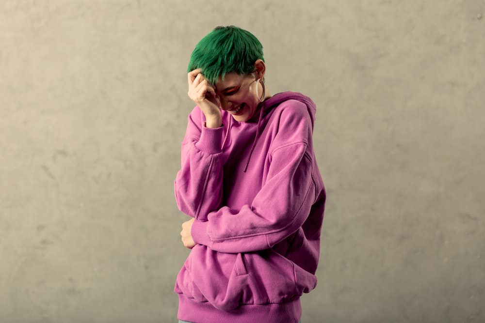 A lady laughing at a friend's joke has fading green hair after using cold water and clarifying shampoos to fade her hair.