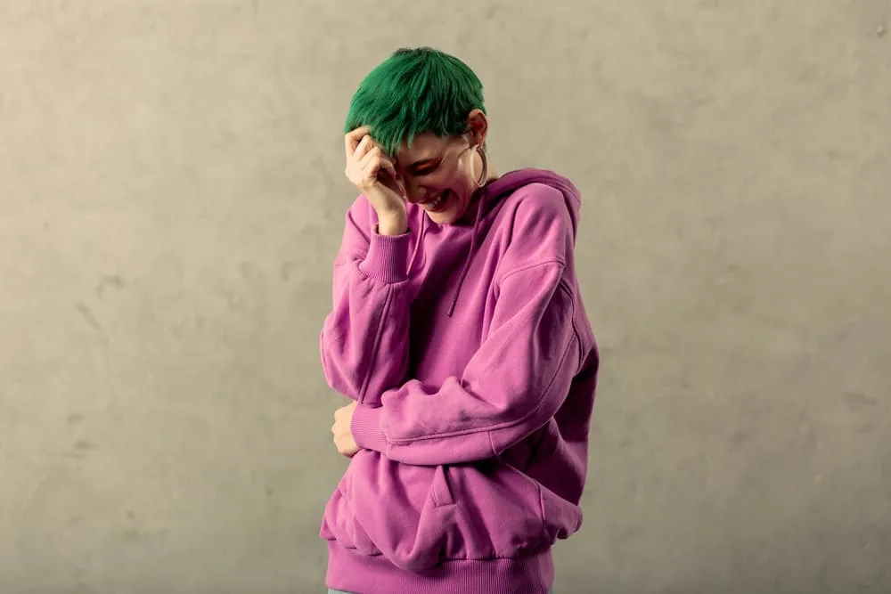 Fading Green Hair: How to Fade Green Dye Fast Step-By-Step 10 A lady laughing at a friend's joke has fading green hair after using cold water and clarifying shampoos to fade her hair.