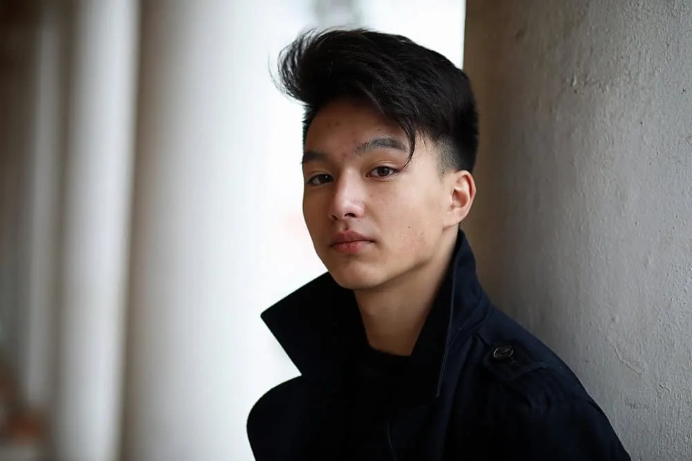 The Best K-Pop Hairstyles for Korean Guys (Plus Styling Tips) 1 A young adult male is wearing popular Korean messy hair that has been brushed forward with a wavy texture.