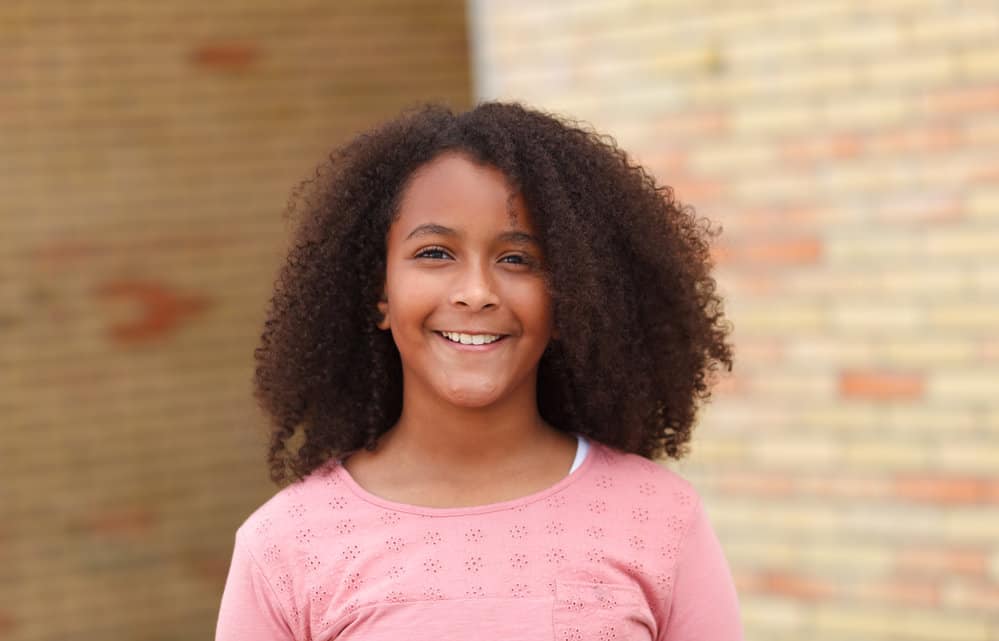 A cute African American little girl with a naturally wavy hair texture has a cute hairstyle with a regular wash-n-go.