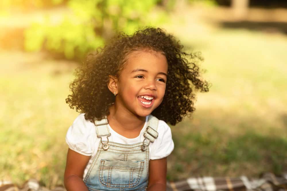 A cute young toddler female, after removing her kids' natural hair braids with purple beads, poses for a photo.