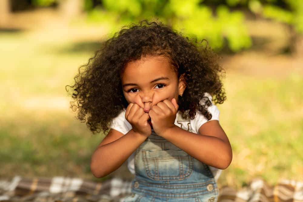 A little girl that recently switched from wearing thin braids with a flower braid design to natural bouncy curls.