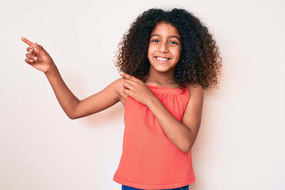 African American girl with natural hair has shoulder hair length curls styled with curl cream for a low maintenance style.