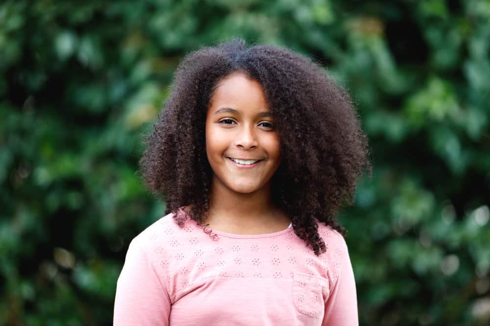 A teenage girl with a great smile has medium hair length on her naturally flowing quick hairstyle.