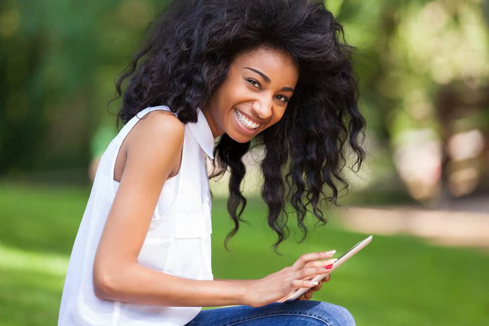 A black girl is sitting outside and wearing a 90s blow-out hairstyle that's common among black teen girls.