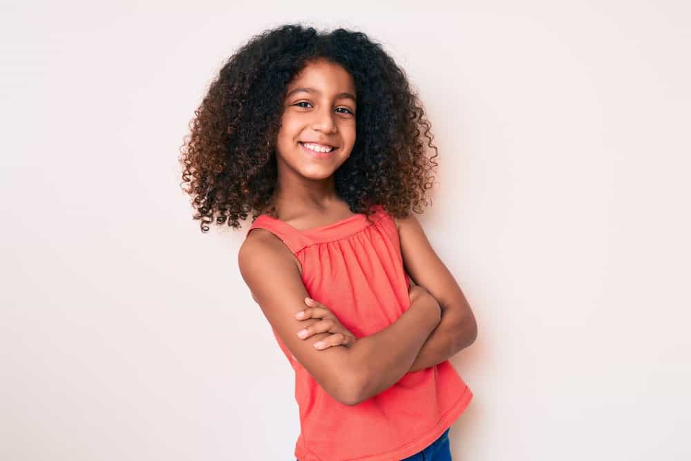 A pretty young black girl with her arms folded after removing long box braids, a simple style for newbies.