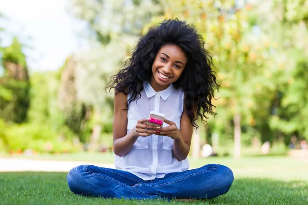 A happy young teenage black girl using an iPhone while wearing a wash-n-go style with bobby pins.