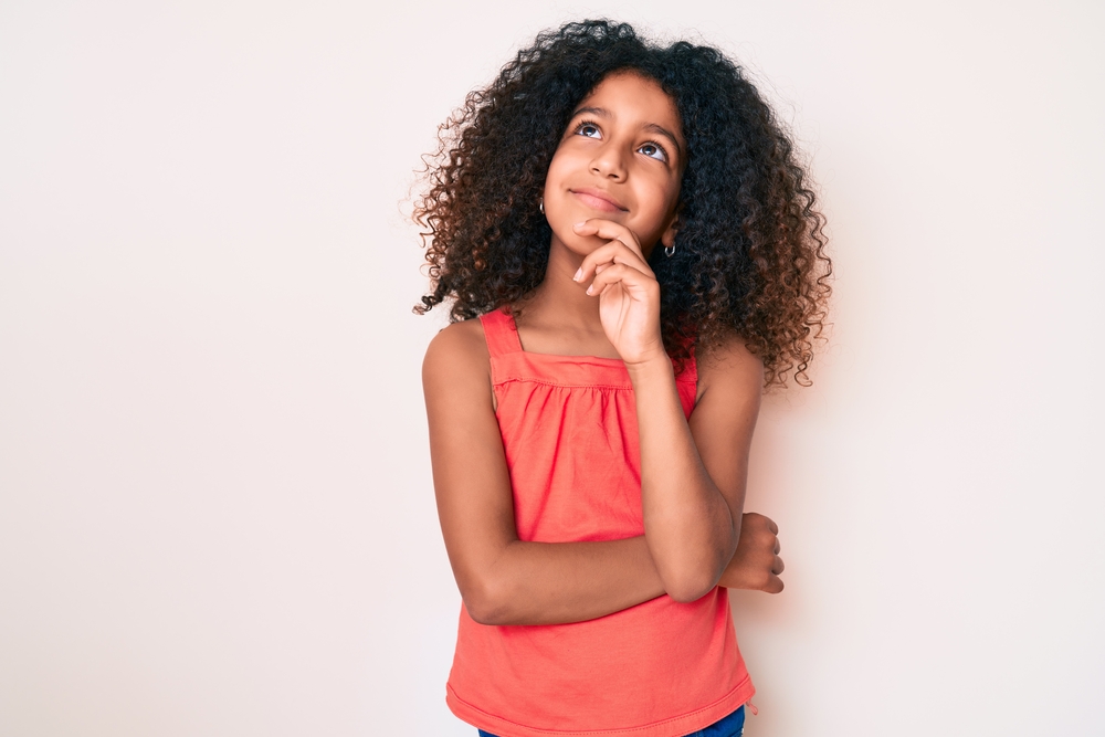 A young black girl with naturally curly black hair is wearing a cute quick hairstyle on a type 3 hair type.