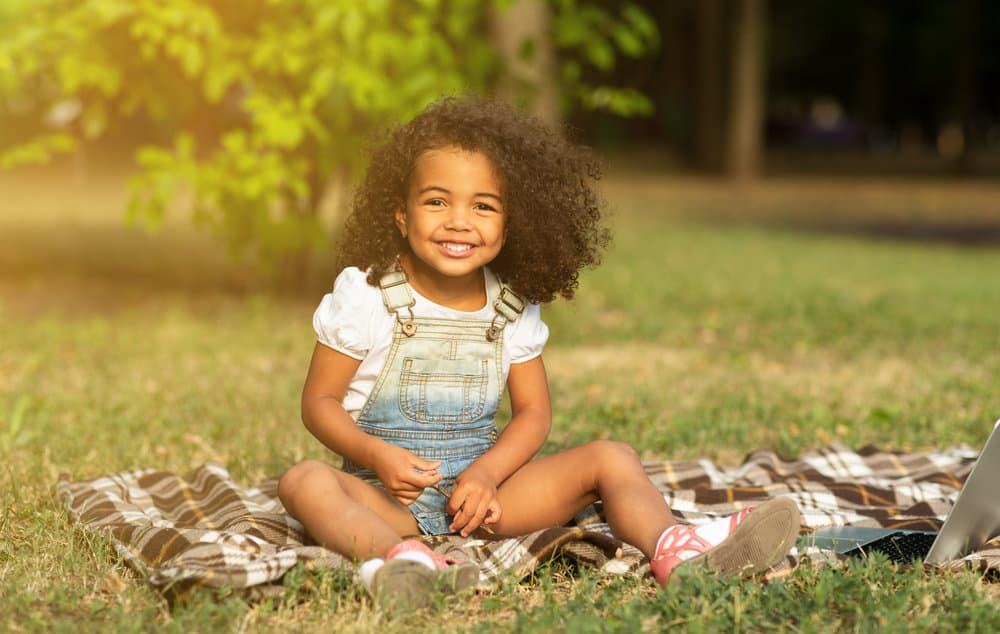 A cute African American girl that is wearing bouncy curls on her type 3 hair type instead of short box braids.