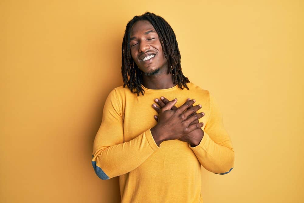 A young African male with a big smile has long hair and is wearing spiky dreads on his type of natural hair texture.