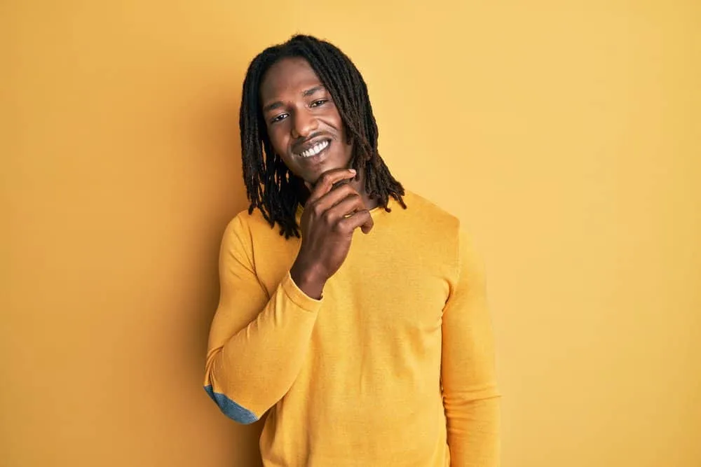 African male with shoulder hair length wearing thin locs on his type 4 curl pattern and a dark yellow casual shirt.
