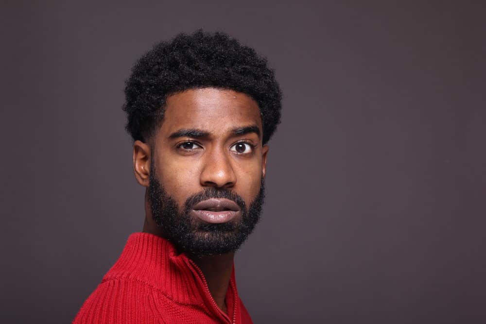 A young man with African American heritage has a growing beard length on his type 4 curly hair follicles.