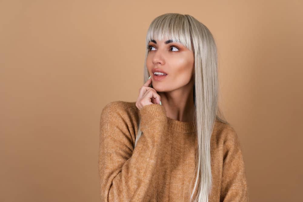 A curious white girl is looking into the distance while wearing a bang hairpiece secured with a bobby pin.