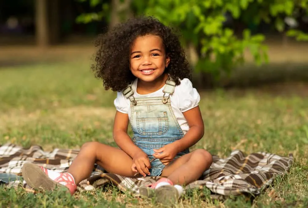 A happy baby girl with beautiful curls is having a picnic in the woods after her mom removes her lovely braids.