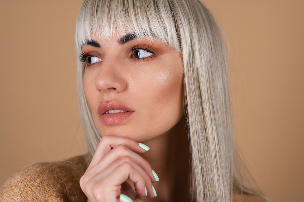 A lady wearing natural-looking makeup with blunt bangs in an awkward stage caused by split ends and breakage.