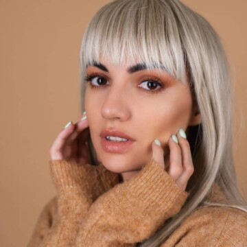 A cute girl with healthy hair wearing fully grown blunt bangs with blonde hair coloring and face-framing layers.