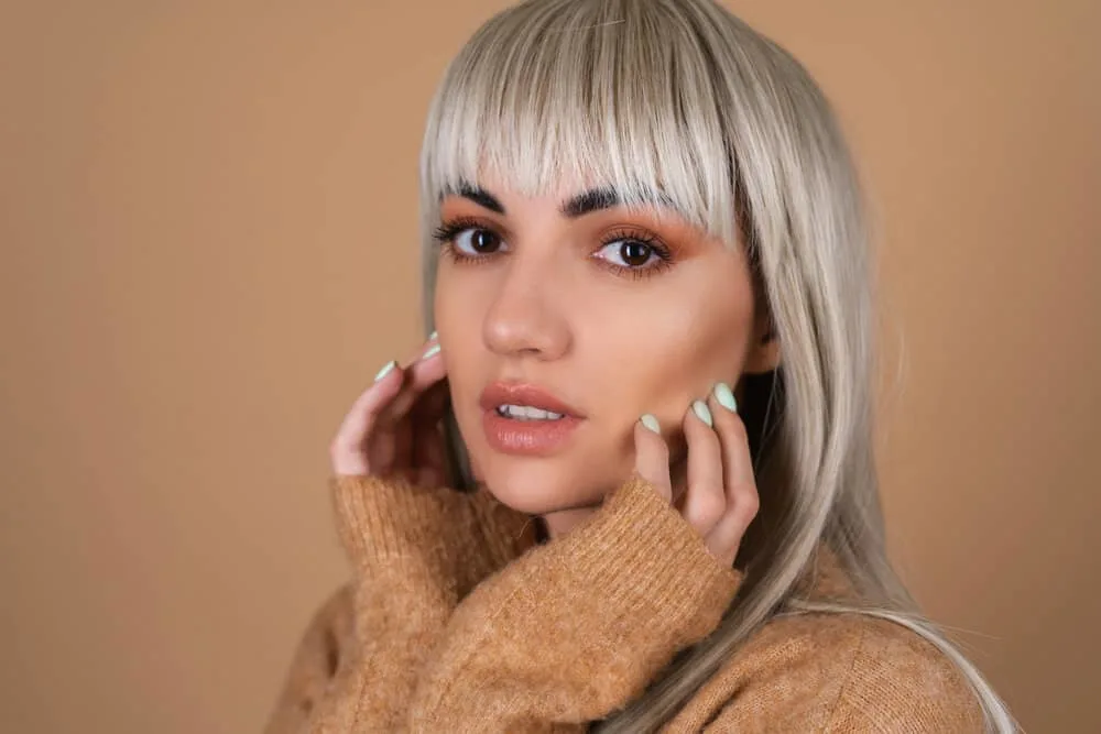 How Long Does It Take for Bangs to Grow Out Fully 1 A cute girl with healthy hair wearing fully grown blunt bangs with blonde hair coloring and face-framing layers.