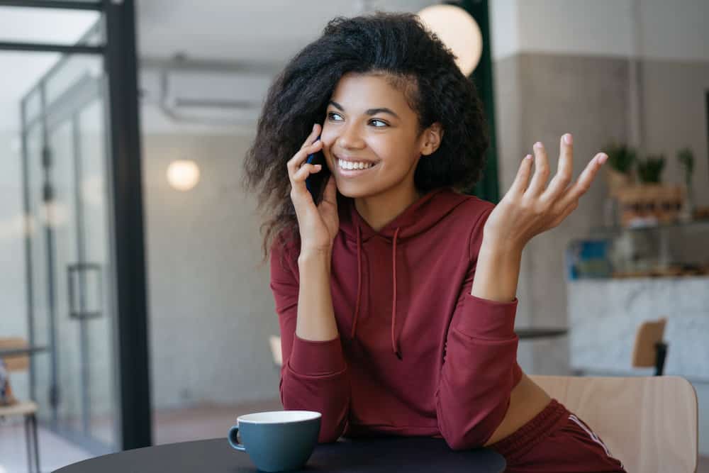 A black girl is talking on the phone to a friend about how BioSilk Hydrating Therapy makes her hair manageable.