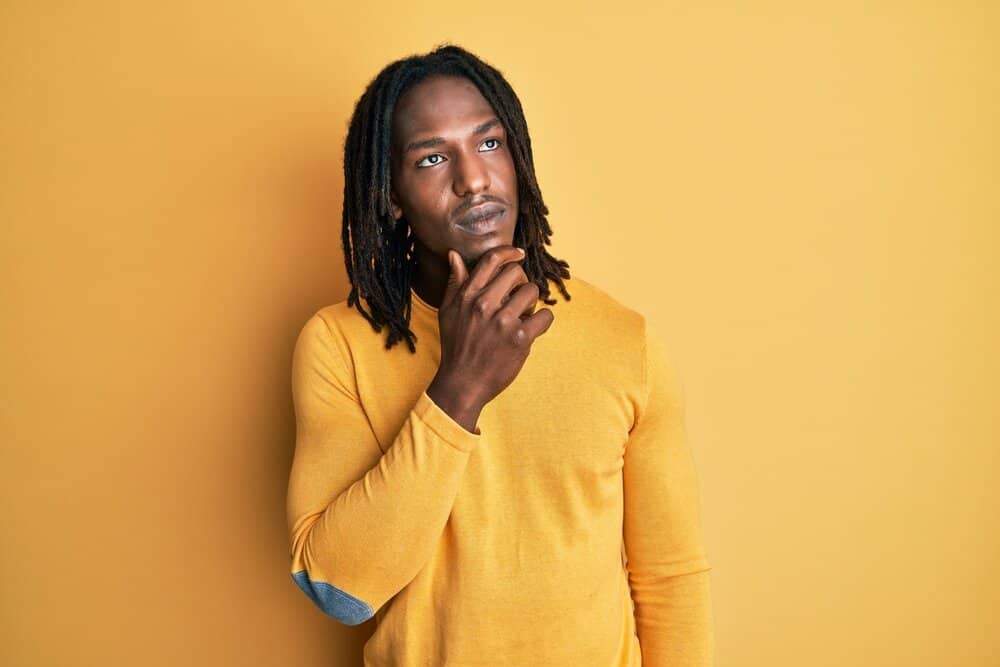 A dark-skinned African American male wearing casual weekend clothing has blooming dreads on type 4 hair strands.